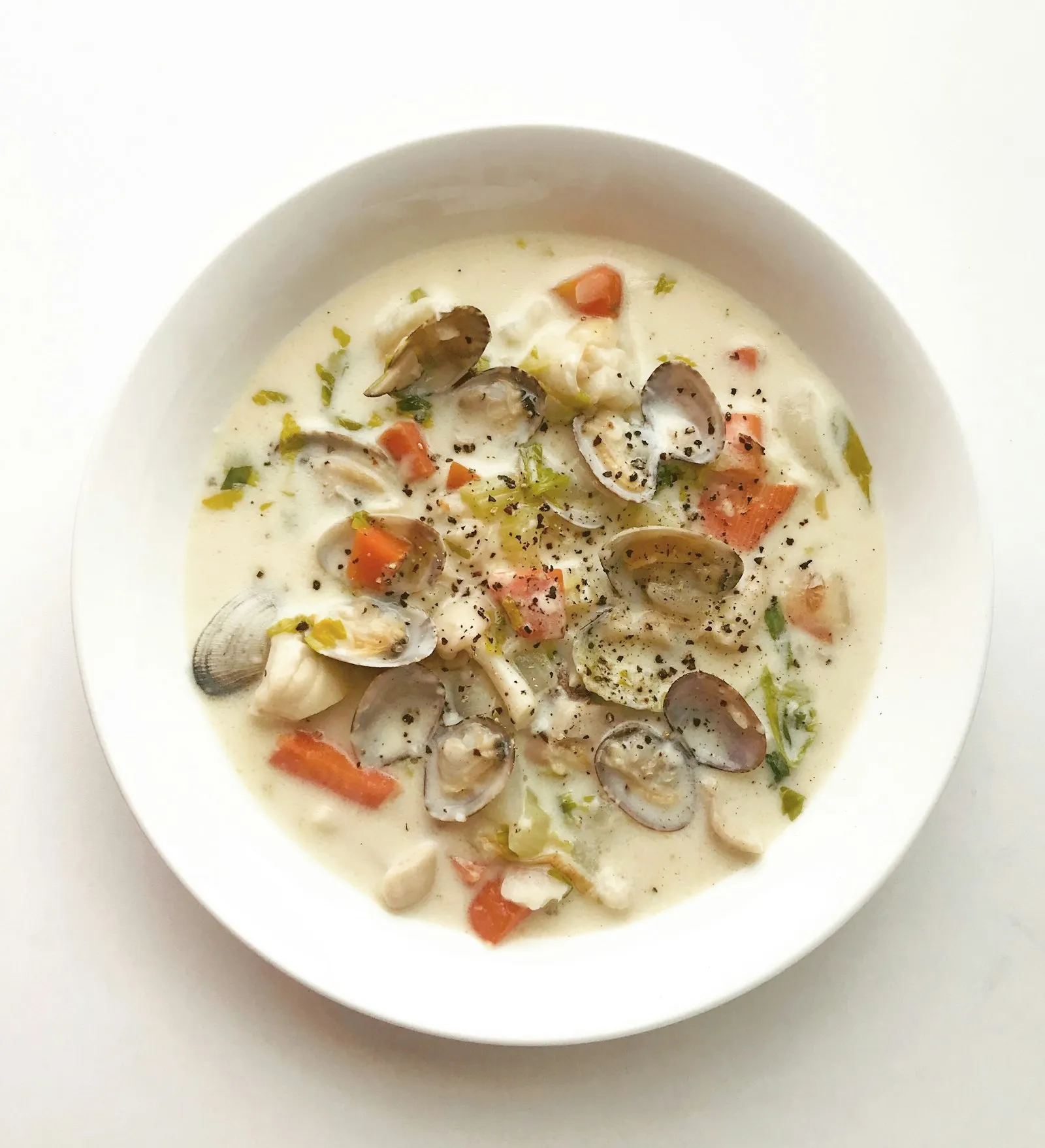 Kremet suppe med skjell, fisk og gulrot i en hvit dyp tallerken